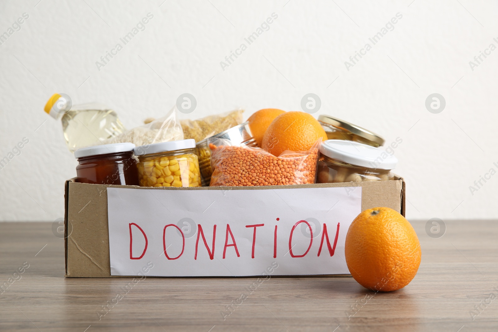 Photo of Different products in cardboard box on wooden table. Food donation