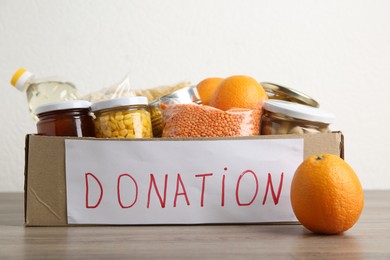 Photo of Different products in cardboard box on wooden table. Food donation