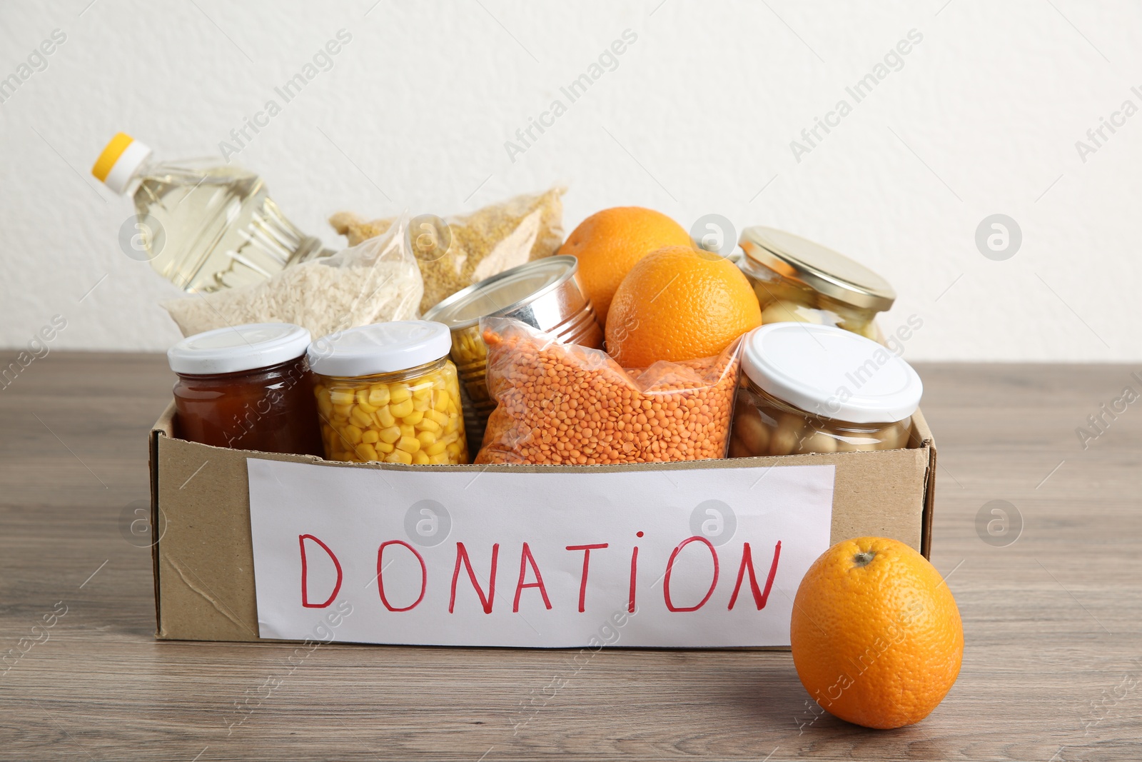 Photo of Different products in cardboard box on wooden table. Food donation