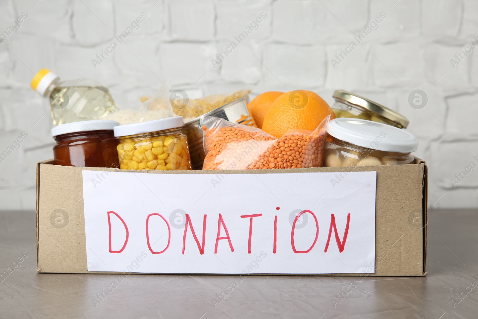 Photo of Different products in cardboard box on grey table. Food donation