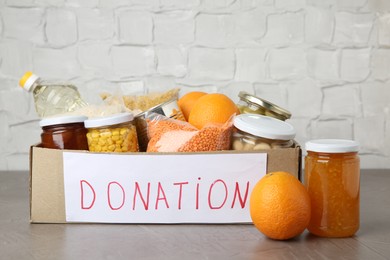 Photo of Different products in cardboard box on grey table. Food donation