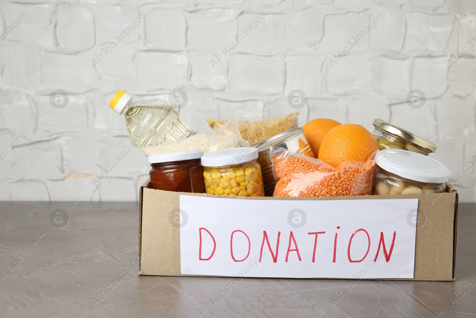 Photo of Different products in cardboard box on grey table. Food donation