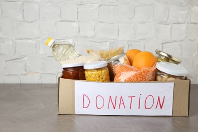 Photo of Different products in cardboard box on grey table. Food donation