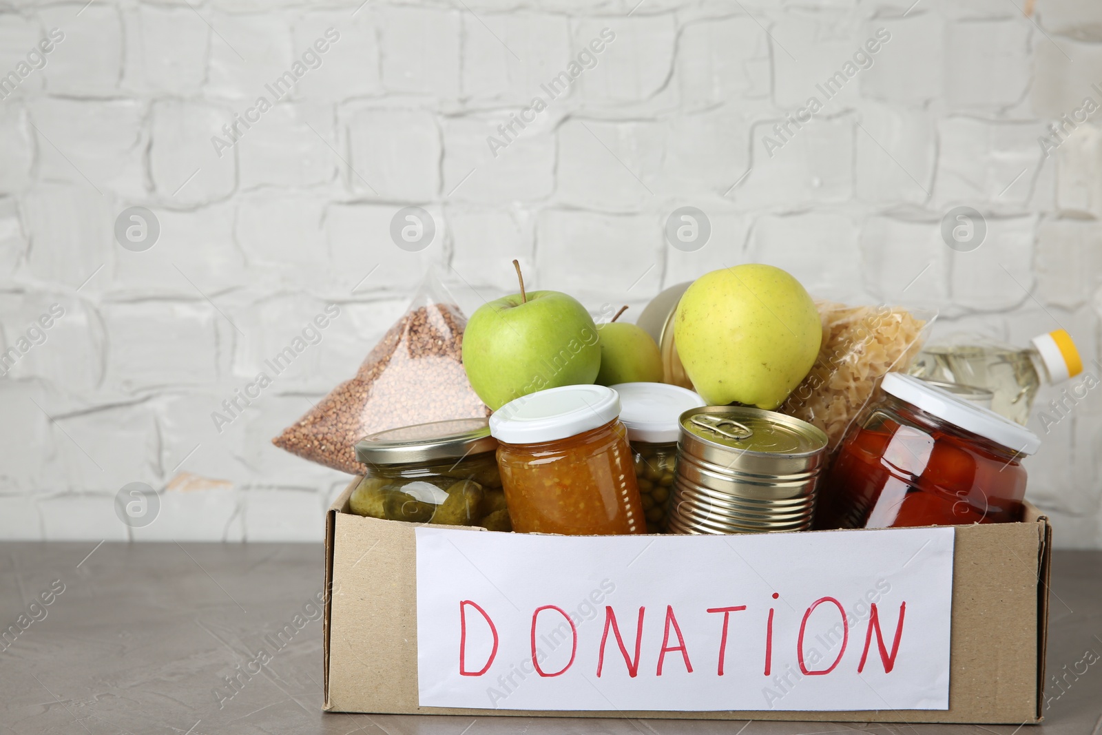 Photo of Different products in cardboard box on grey table. Food donation