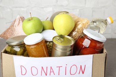 Photo of Donation food products in cardboard box on grey table, closeup