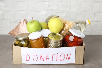 Photo of Donation food products in cardboard box on grey table