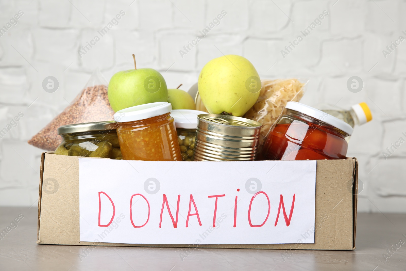 Photo of Donation food products in cardboard box on grey table