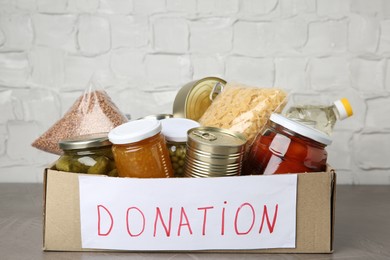 Photo of Donation food products in cardboard box on grey table