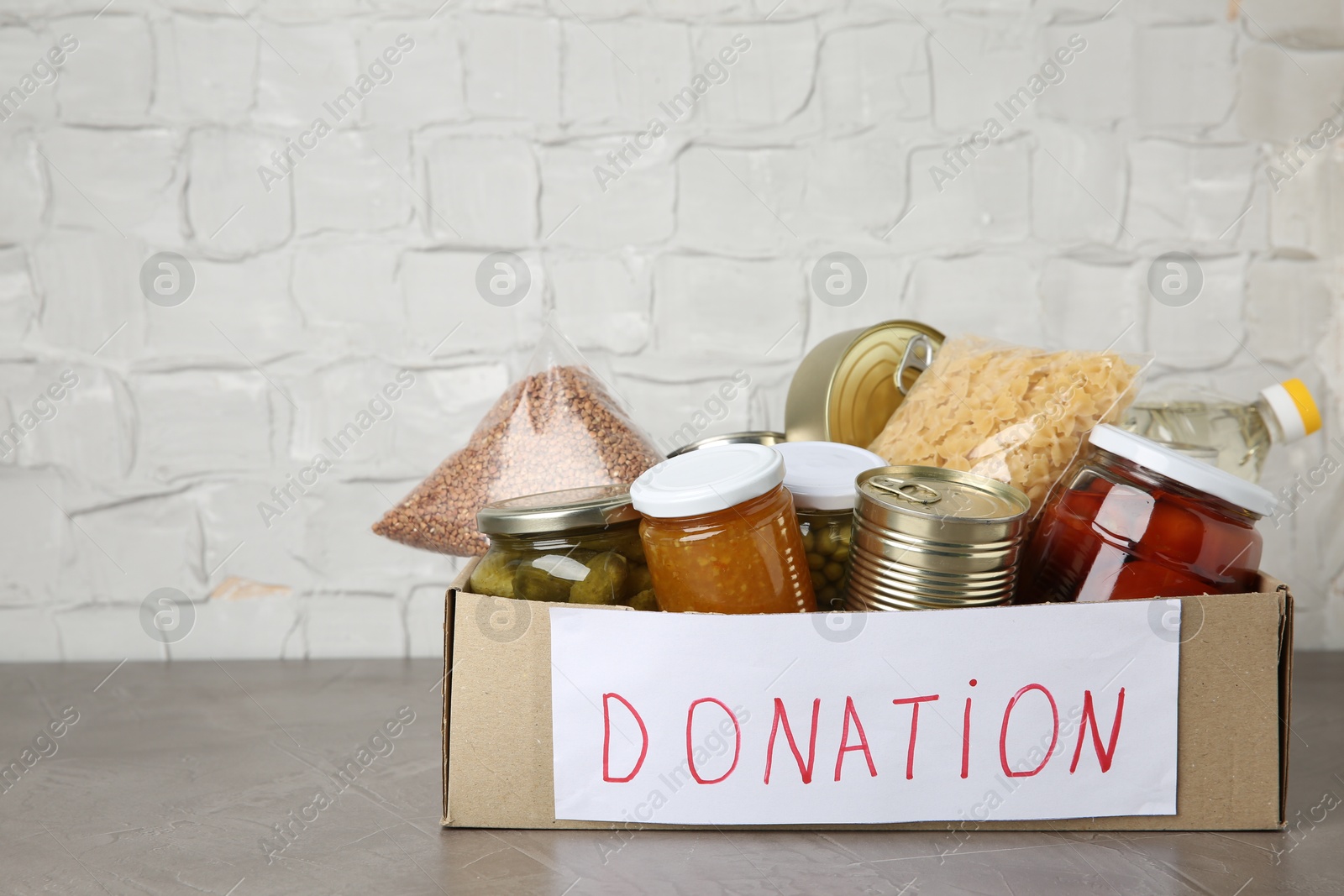 Photo of Donation food products in cardboard box on grey table. Space for text