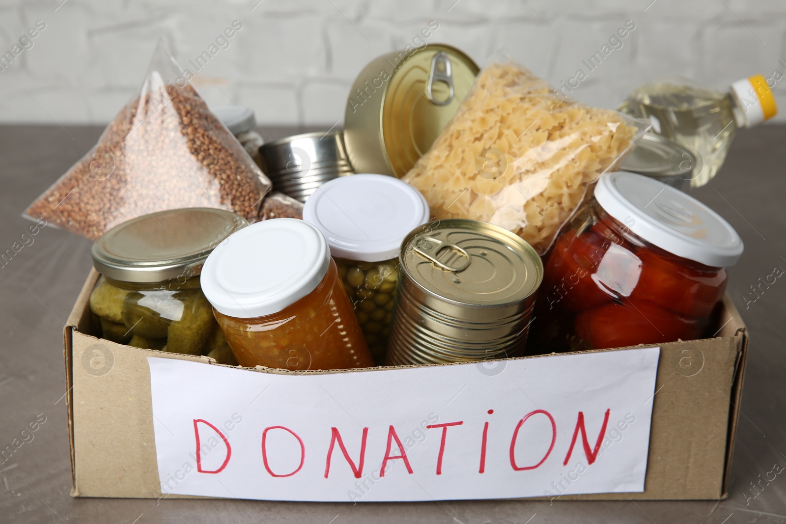 Photo of Donation food products in cardboard box on grey table, closeup