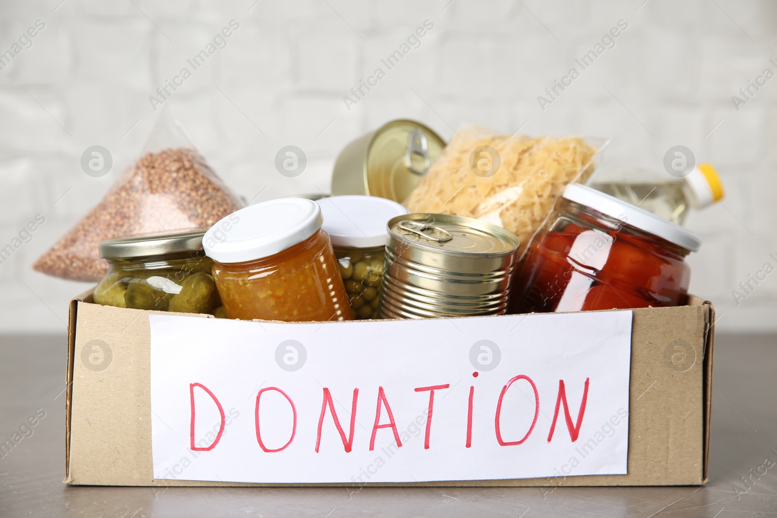 Photo of Donation food products in cardboard box on grey table, closeup