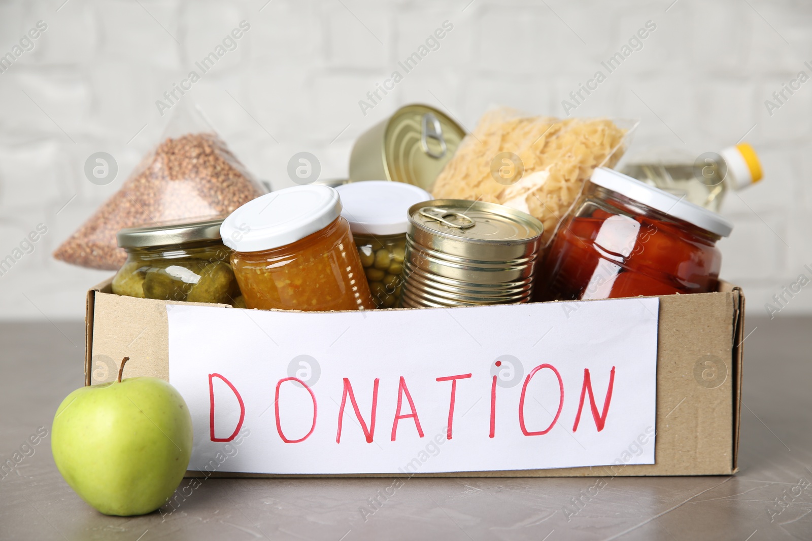 Photo of Donation food products in cardboard box on grey table, closeup