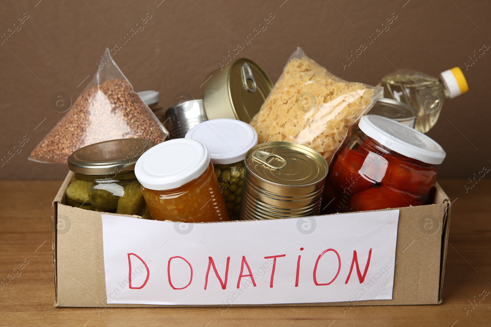 Photo of Donation food products in cardboard box on wooden table