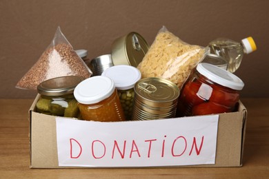 Photo of Donation food products in cardboard box on wooden table