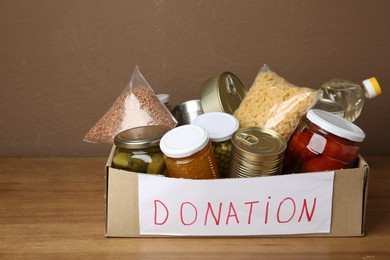 Photo of Donation food products in cardboard box on wooden table