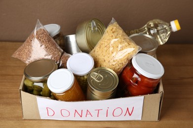 Photo of Donation food products in cardboard box on wooden table