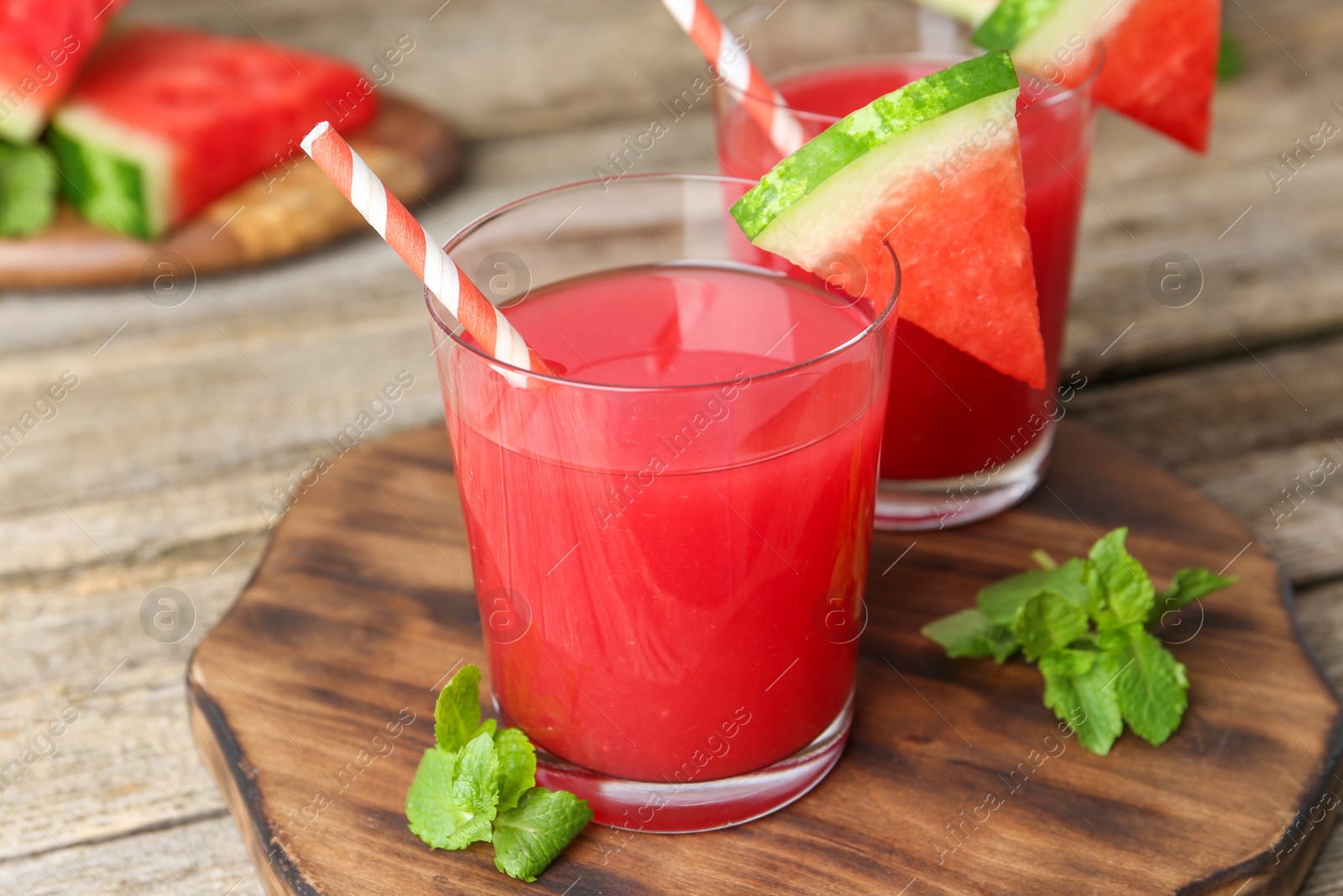 Photo of Tasty watermelon drink in glasses, fresh fruit and mint on wooden table, closeup