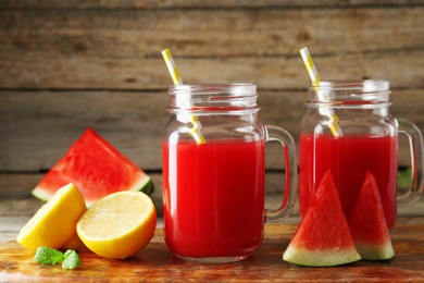 Photo of Tasty watermelon drink in mason jars and fresh fruits on wooden table, closeup