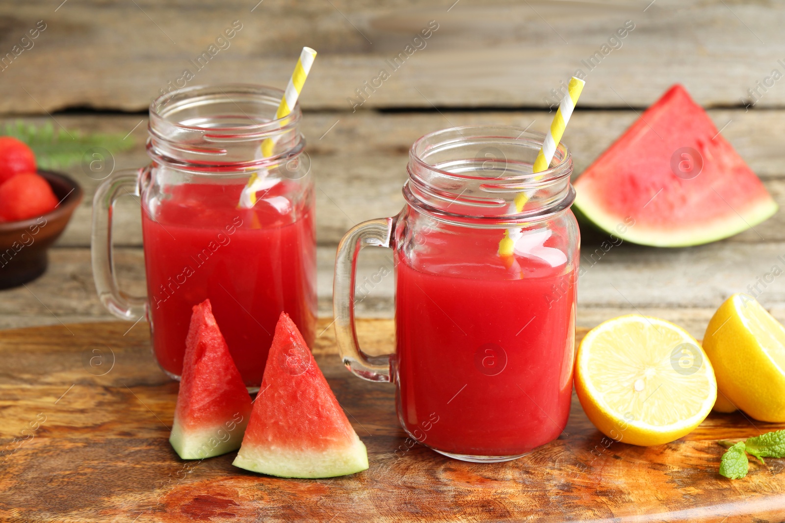 Photo of Tasty watermelon drink in mason jars and fresh fruits on wooden table, closeup