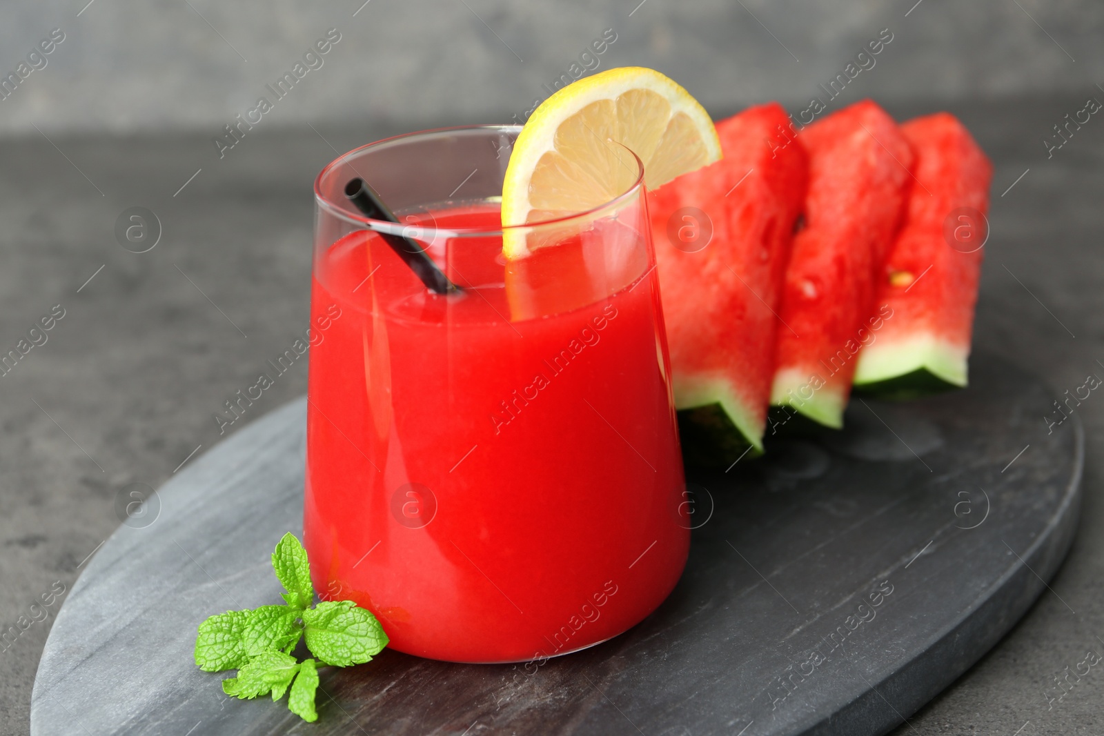 Photo of Tasty watermelon drink in glass, fresh fruits and mint on grey table, closeup