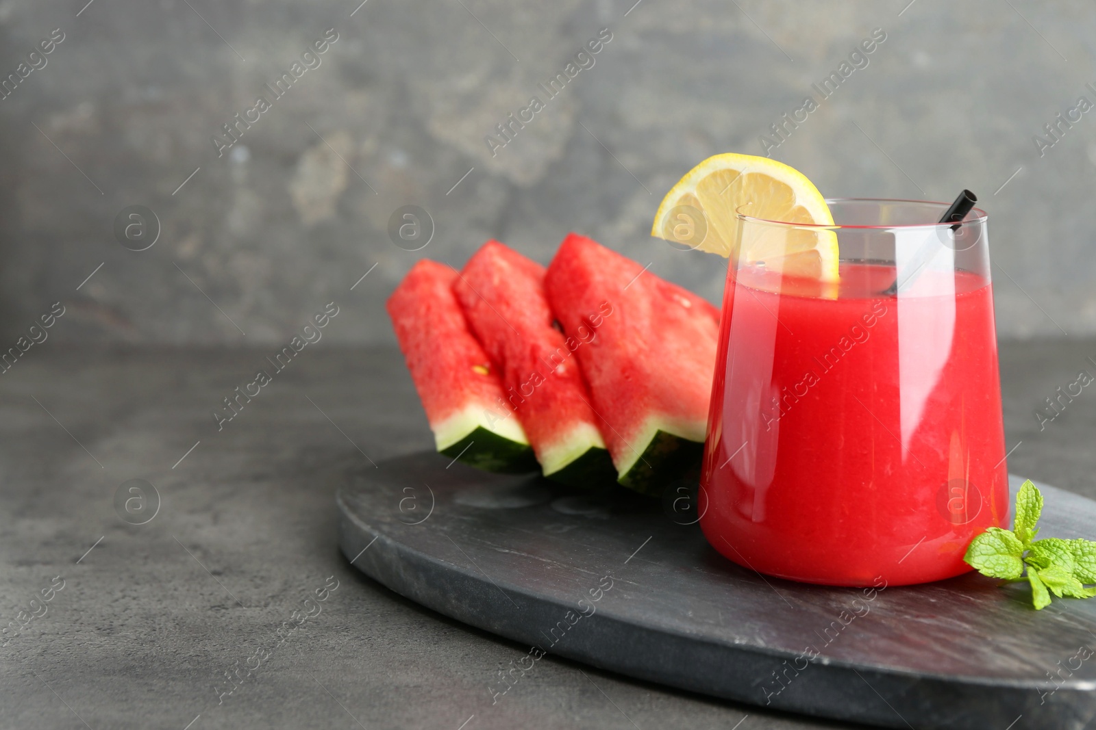 Photo of Tasty watermelon drink in glass, fresh fruits and mint on grey table. Space for text