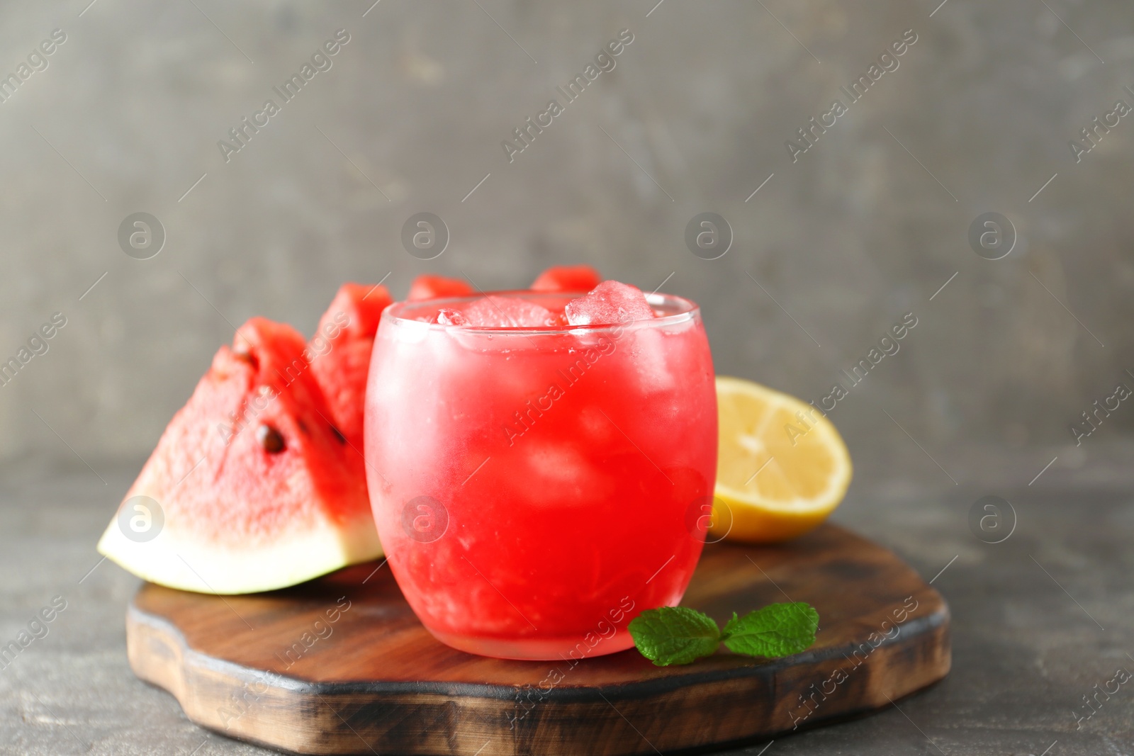 Photo of Tasty watermelon drink in glass, fresh fruits and mint on grey table, closeup