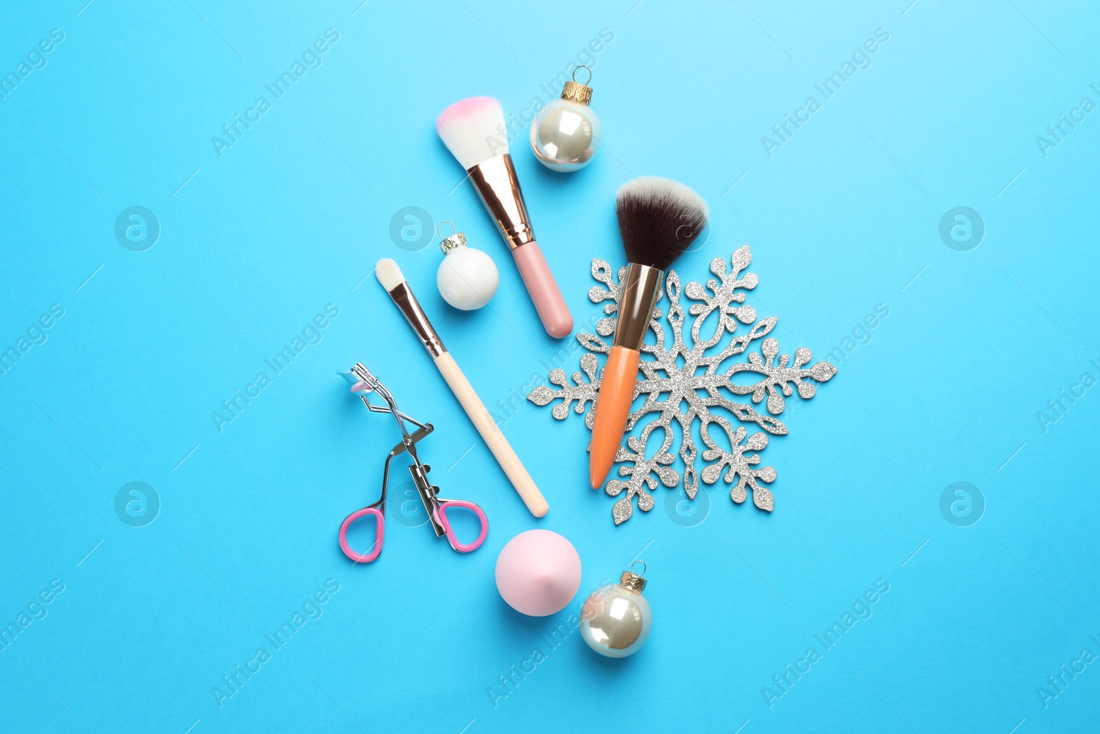 Photo of Makeup brushes, eyelash curler and Christmas decor on light blue background, flat lay