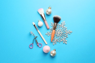 Photo of Makeup brushes, eyelash curler and Christmas decor on light blue background, flat lay