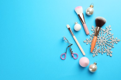 Photo of Makeup brushes, eyelash curler and Christmas decor on light blue background, flat lay. Space for text