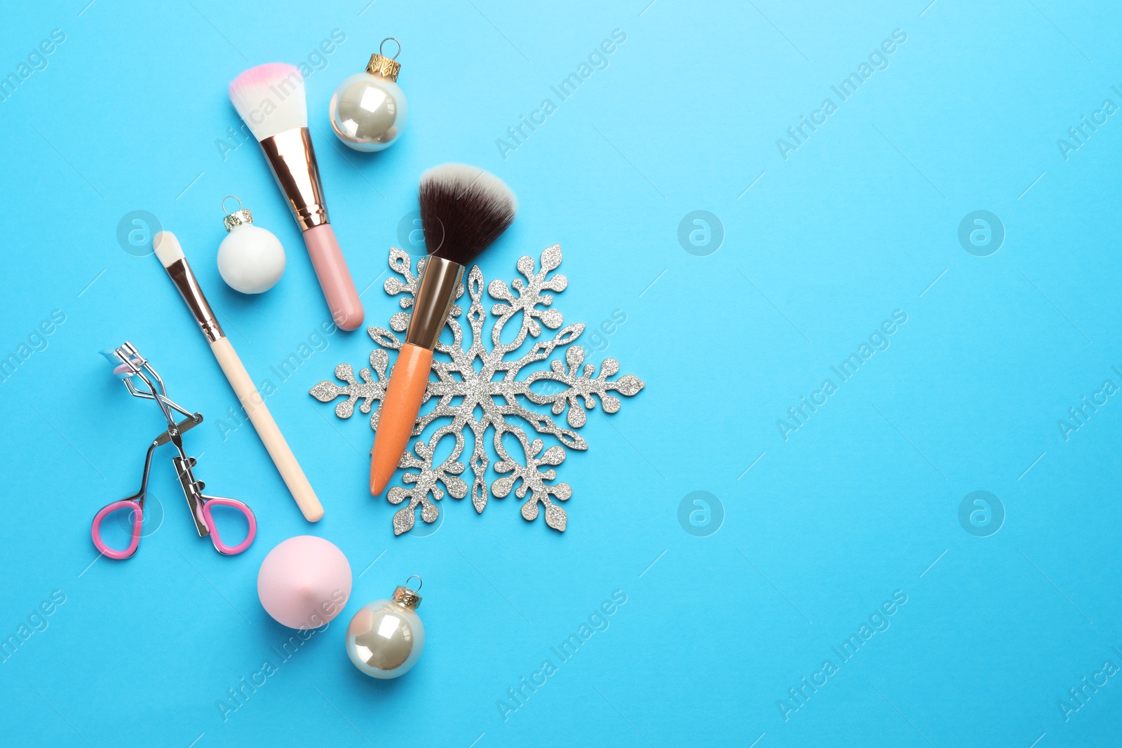 Photo of Makeup brushes, eyelash curler and Christmas decor on light blue background, flat lay. Space for text