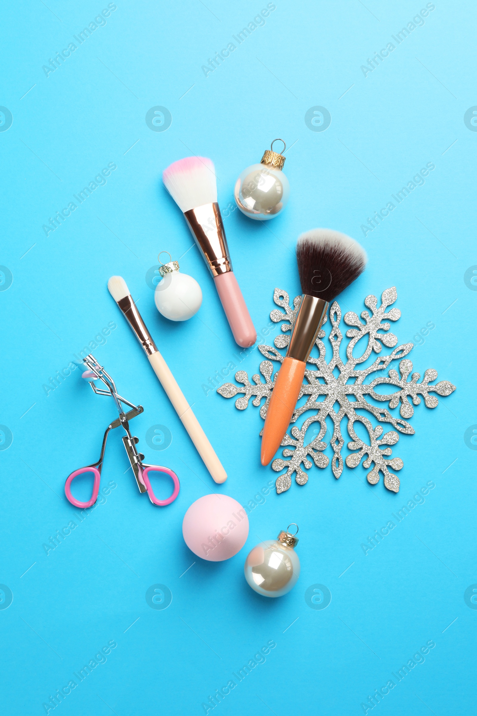 Photo of Makeup brushes, eyelash curler and Christmas decor on light blue background, flat lay