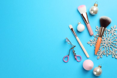 Photo of Makeup brushes, eyelash curler and Christmas decor on light blue background, flat lay. Space for text