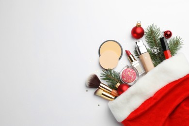 Photo of Santa hat with different decorative cosmetic products and Christmas decor on white background, top view. Space for text