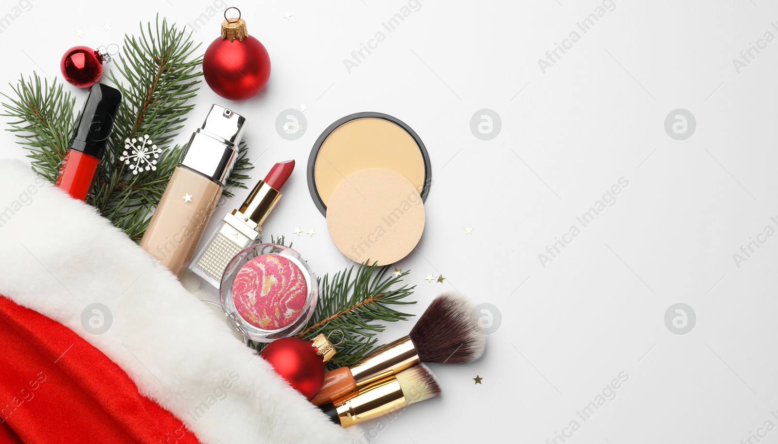 Photo of Santa hat with different decorative cosmetic products and Christmas decor on white background, top view. Space for text