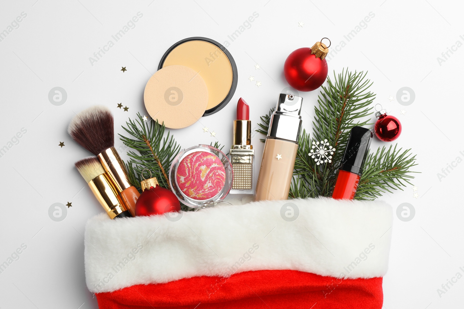 Photo of Santa hat with different decorative cosmetic products and Christmas decor on white background, top view