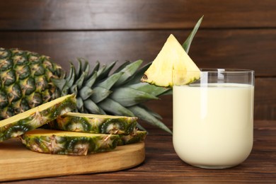 Photo of Tasty pineapple smoothie in glass and slices of fruit on wooden table, closeup