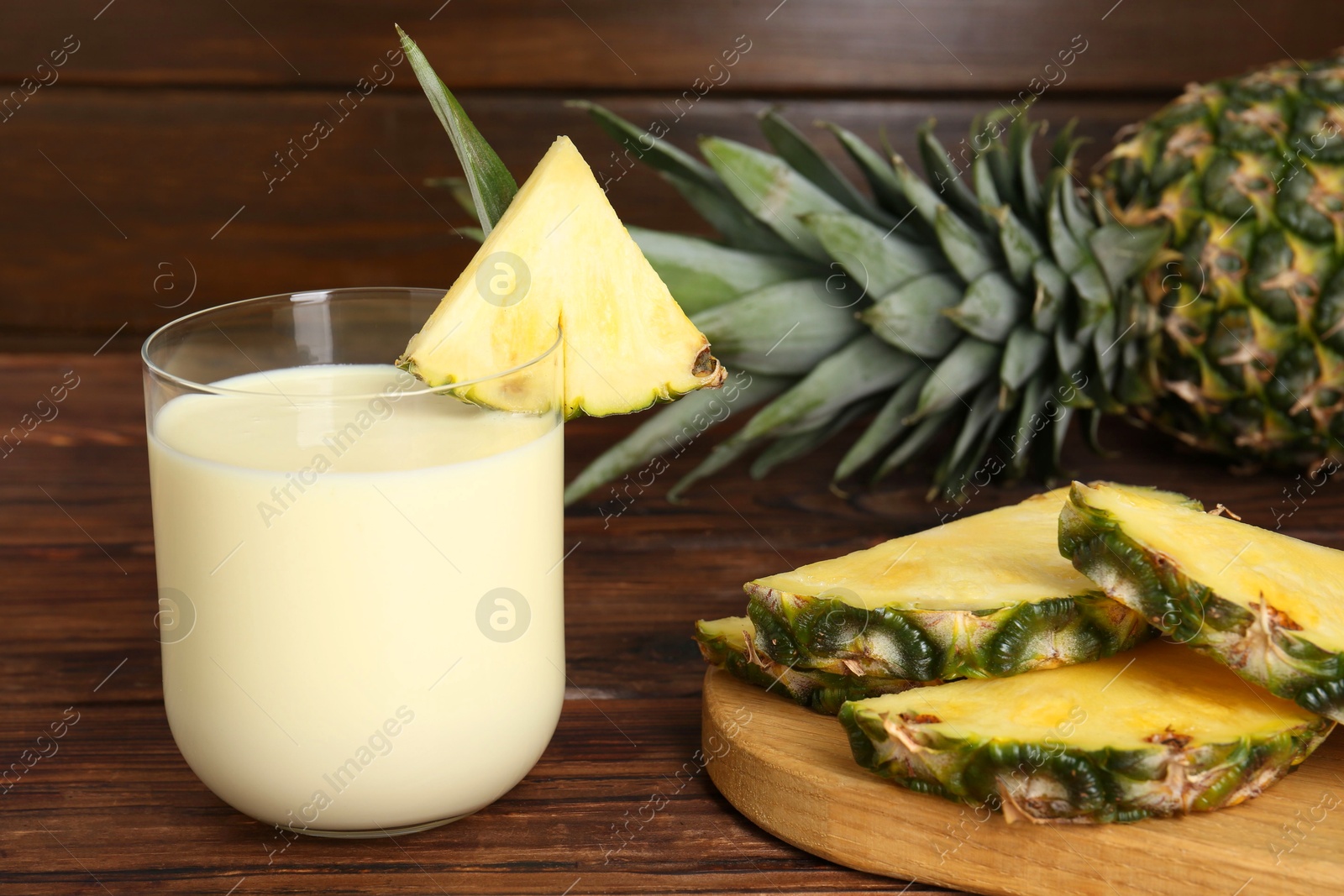 Photo of Tasty pineapple smoothie in glass and slices of fruit on wooden table, closeup