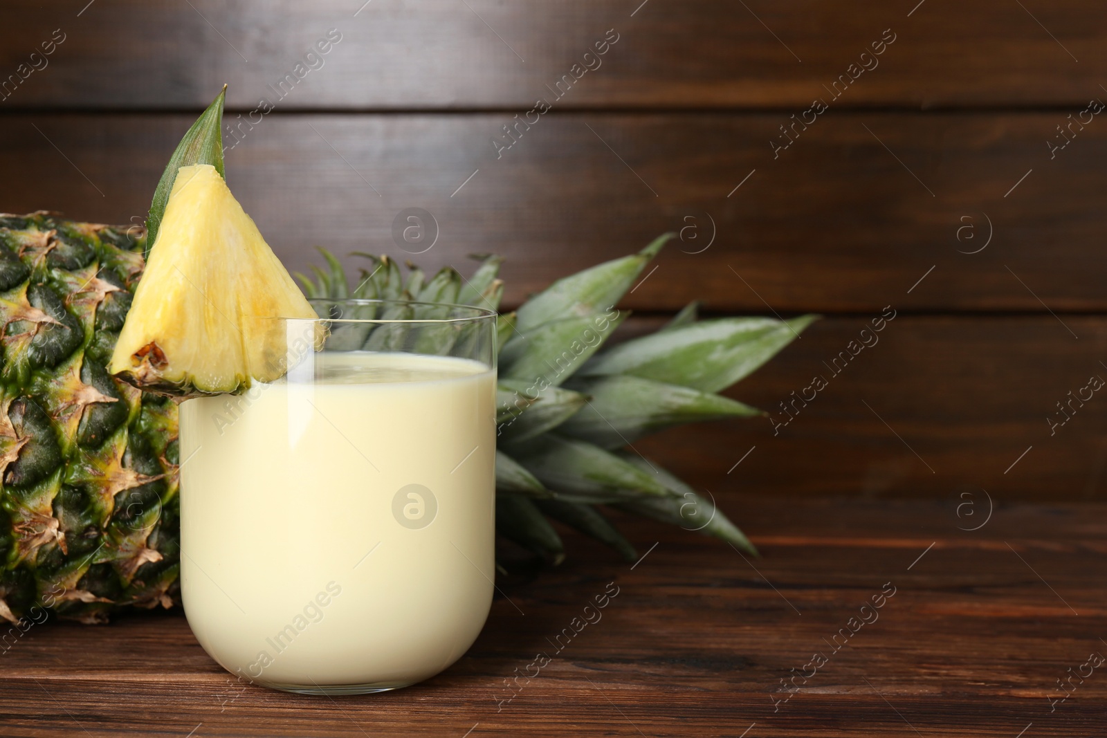 Photo of Tasty pineapple smoothie in glass and of fruit on wooden table, closeup. Space for text