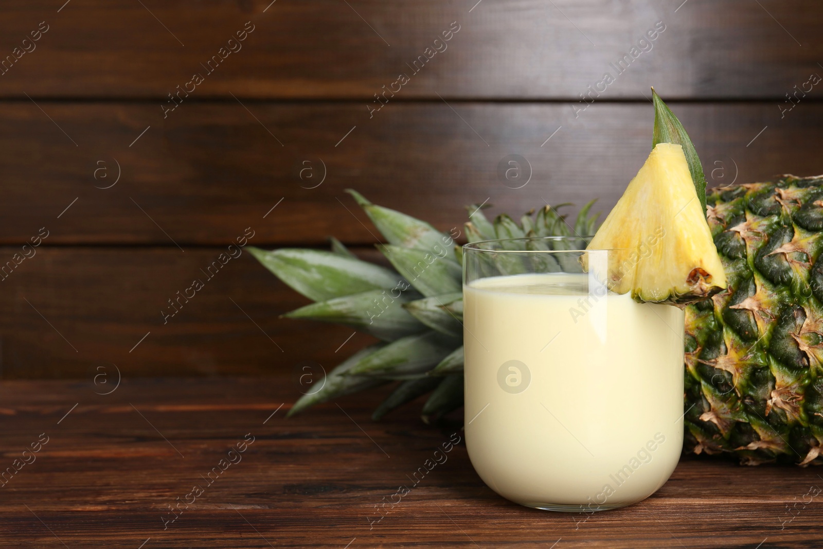 Photo of Tasty pineapple smoothie in glass and of fruit on wooden table, closeup. Space for text