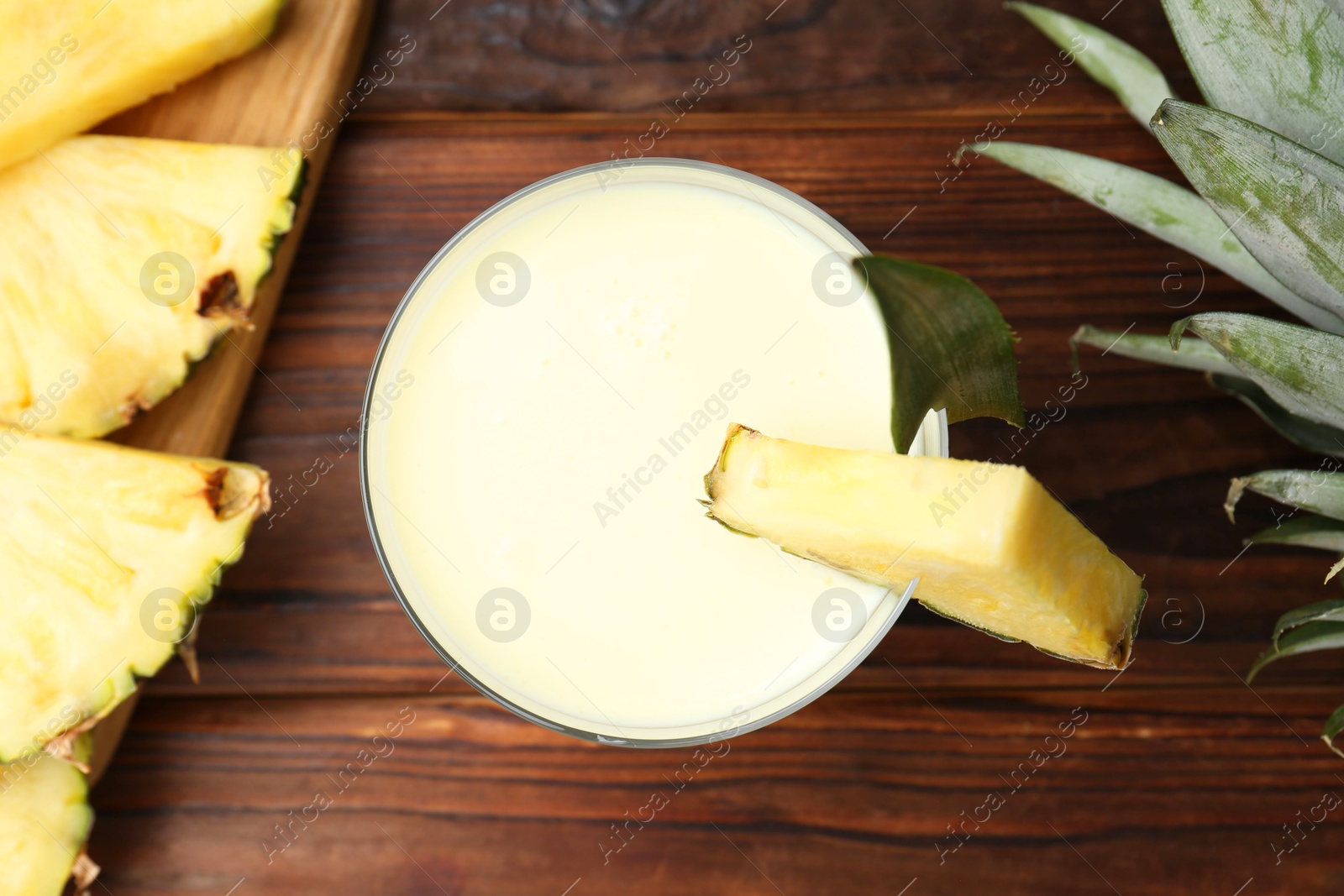 Photo of Tasty pineapple smoothie in glass, leaves and slices of fruit on wooden table, flat lay