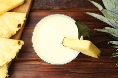 Photo of Tasty pineapple smoothie in glass, leaves and slices of fruit on wooden table, flat lay