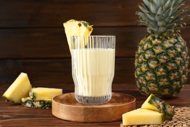 Photo of Tasty pineapple smoothie in glass and slices of fruit on wooden table, closeup