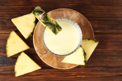 Photo of Tasty pineapple smoothie in glass and slices of fruit on wooden table, flat lay