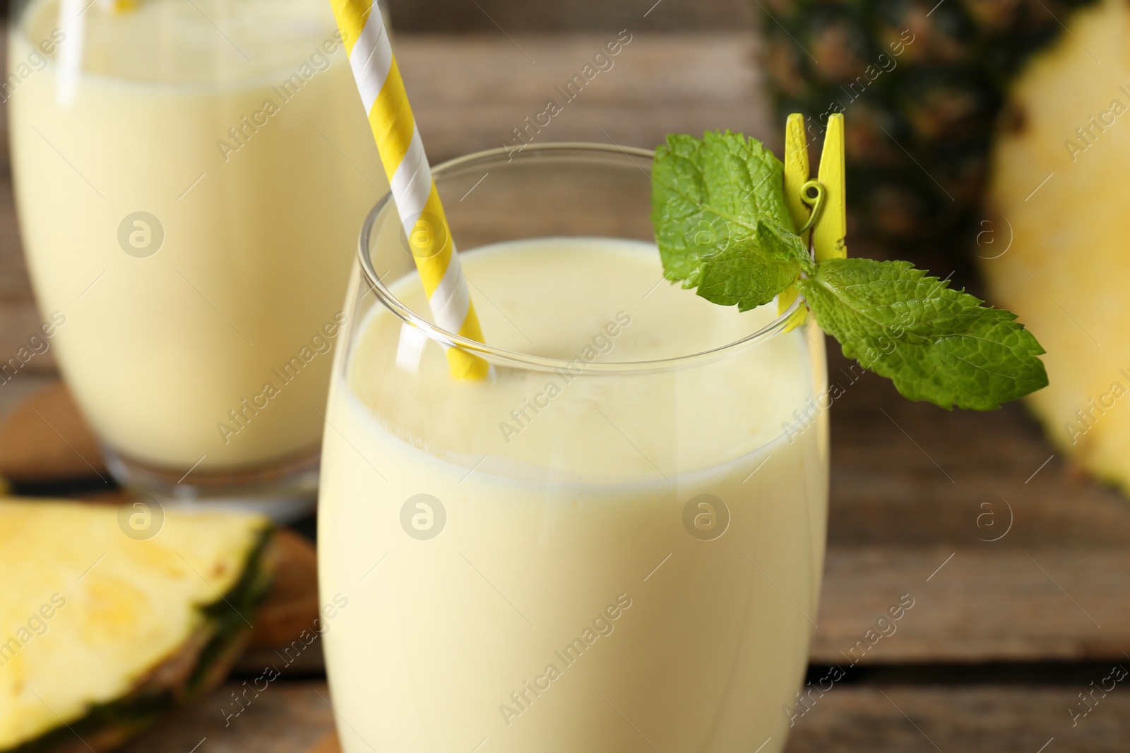 Photo of Tasty pineapple smoothie in glasses, mint and fruit on wooden table, closeup