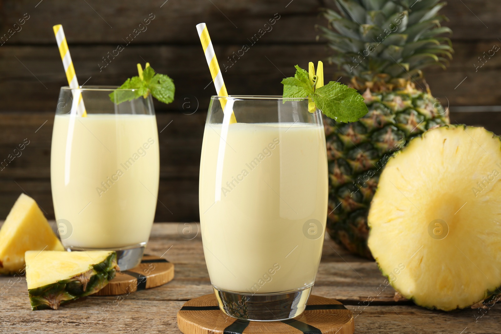 Photo of Tasty pineapple smoothie in glasses, mint and fruit on wooden table, closeup