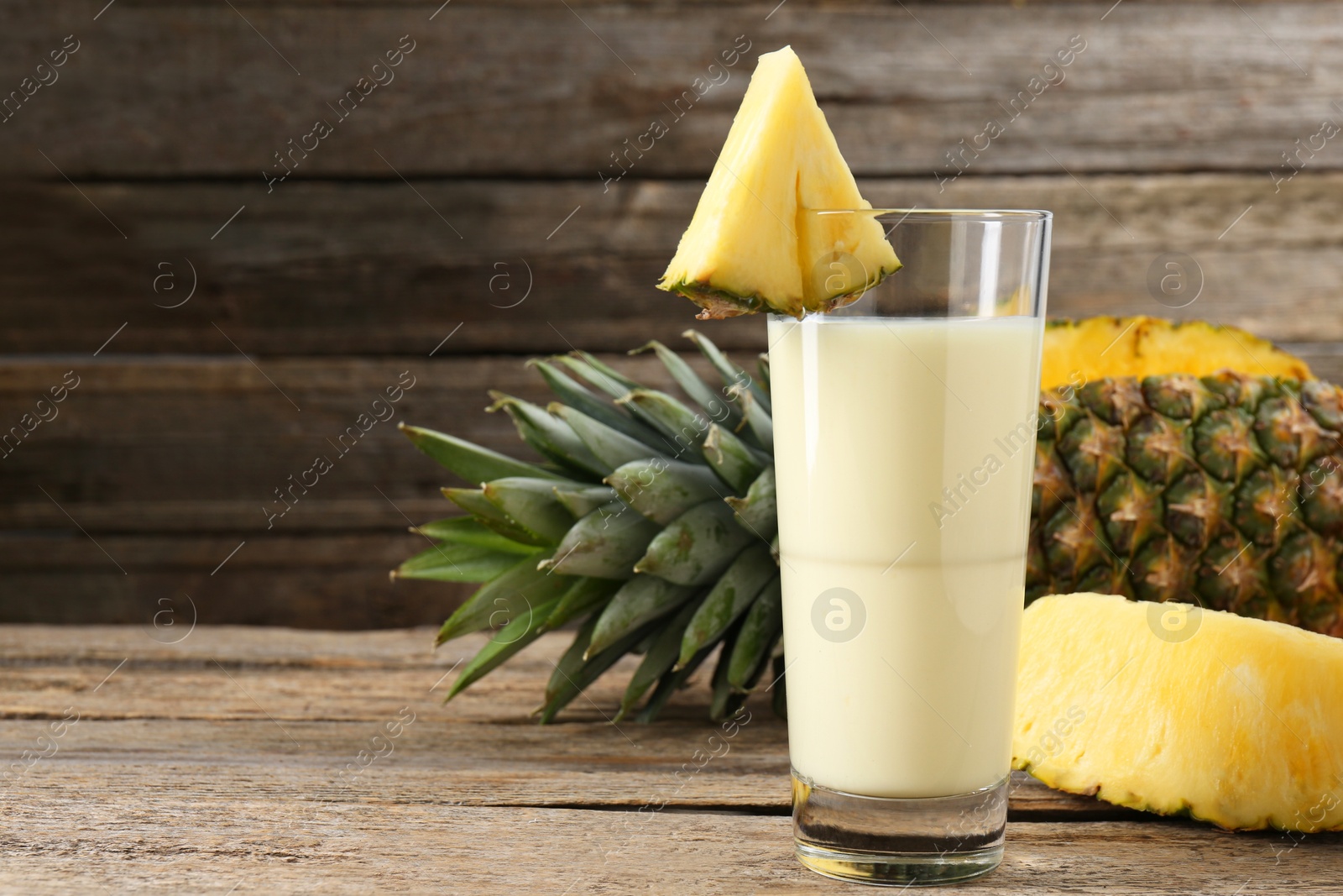 Photo of Tasty pineapple smoothie in glass and fruit on wooden table, closeup. Space for text