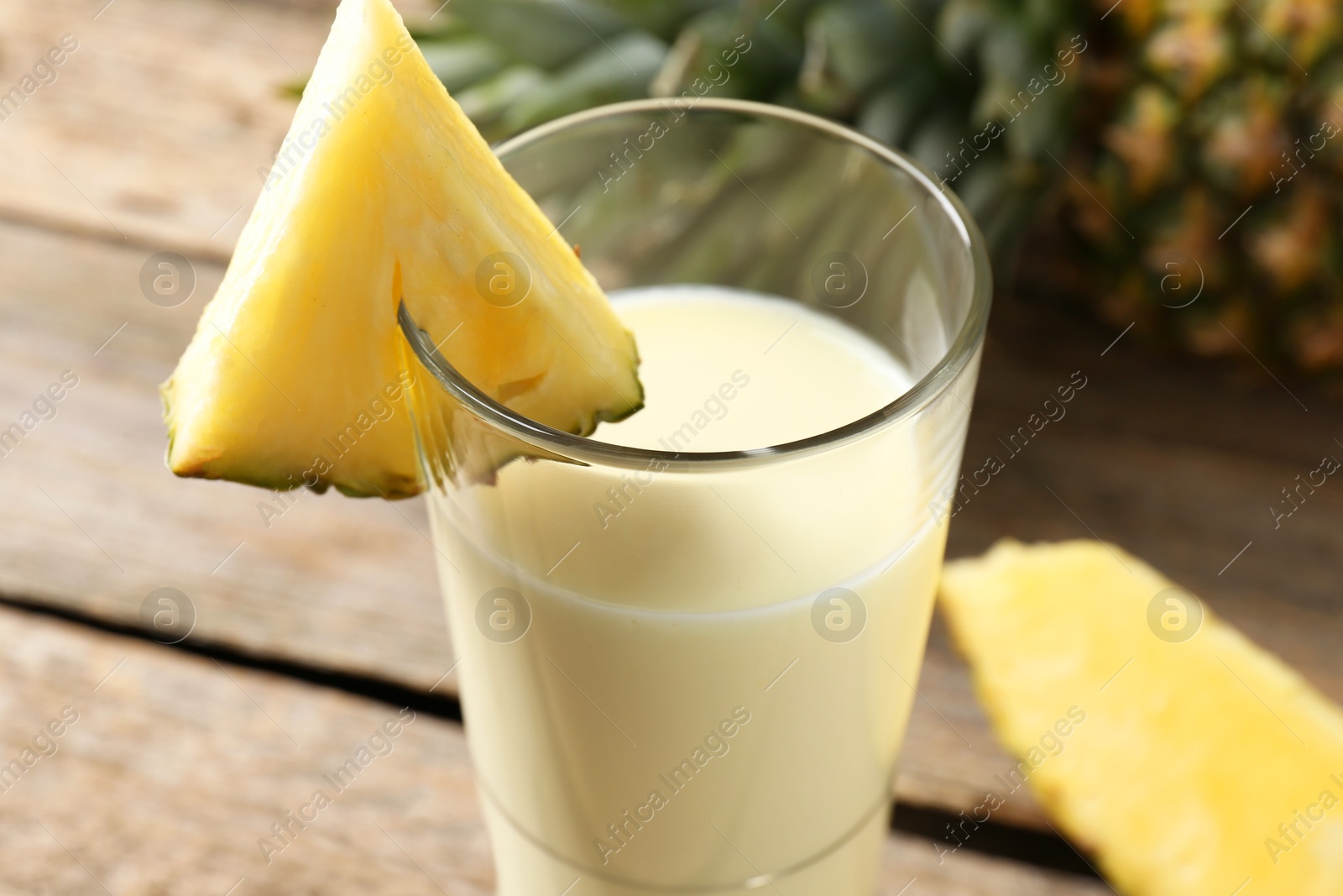 Photo of Tasty pineapple smoothie in glass and fruit on table, closeup