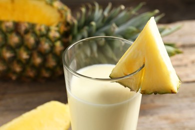 Photo of Tasty pineapple smoothie in glass and fruit on table, closeup