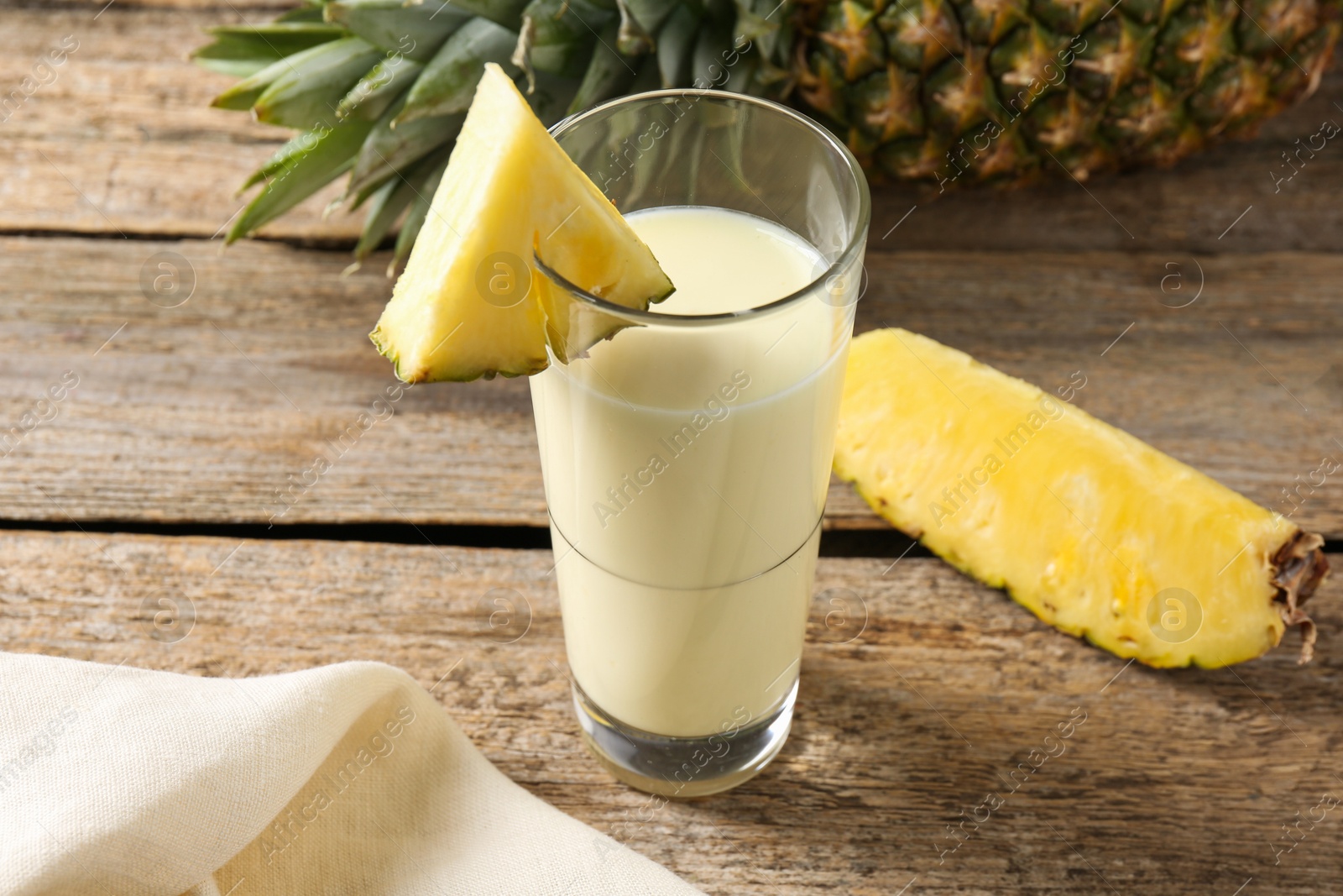 Photo of Tasty pineapple smoothie in glass and fruit on wooden table, closeup