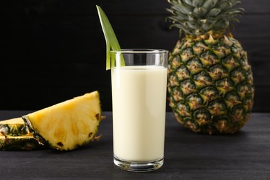 Photo of Tasty pineapple smoothie in glass and fruit on black wooden table, closeup